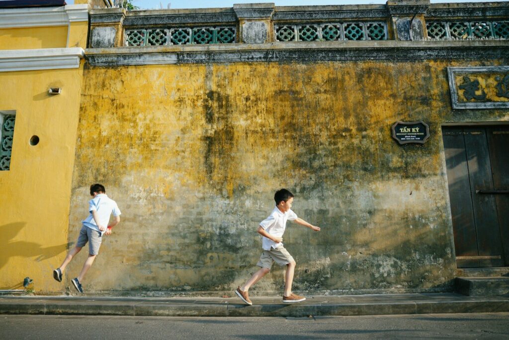 two boys are running down the street in front of a yellow building